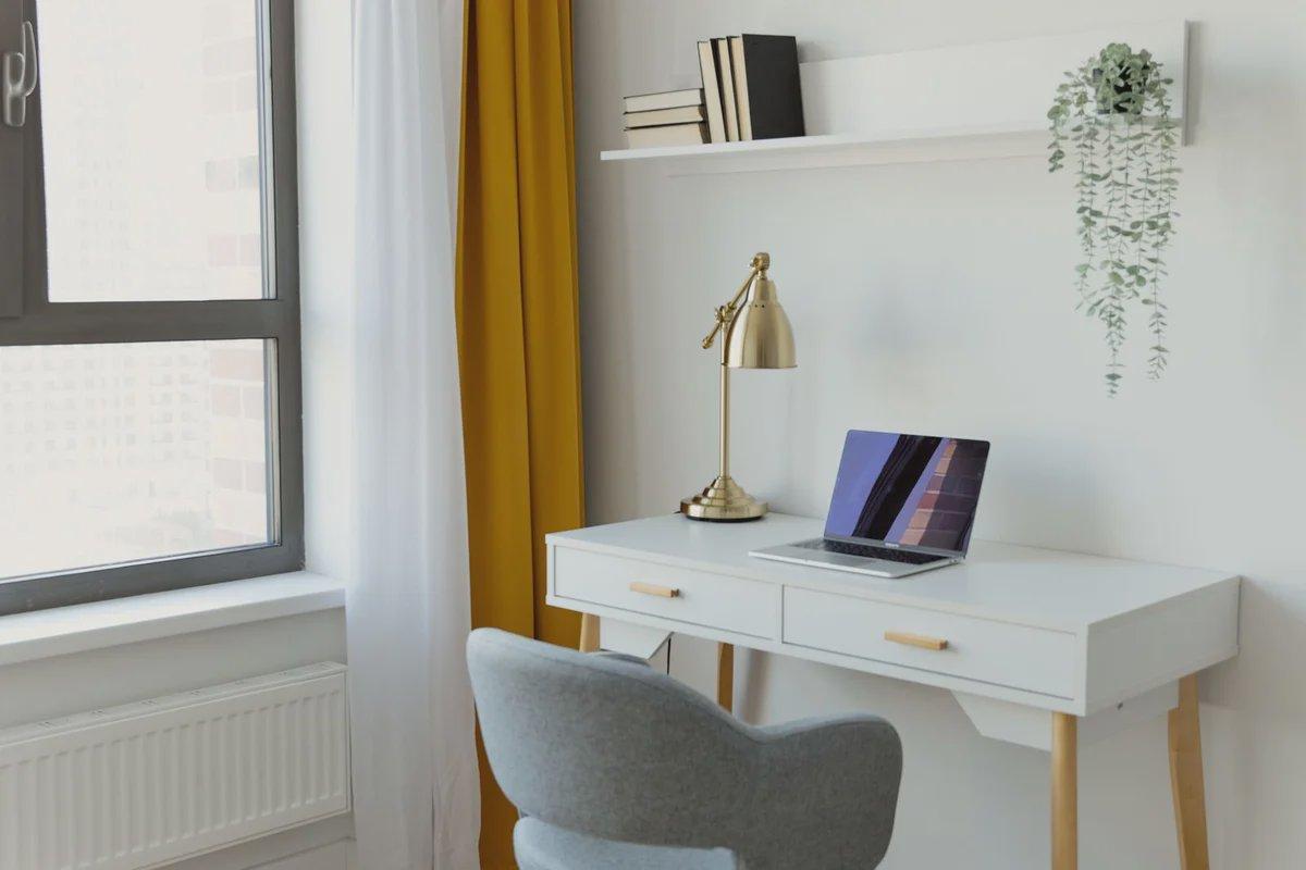 A laptop rests on a white desk beside a sunlit window.