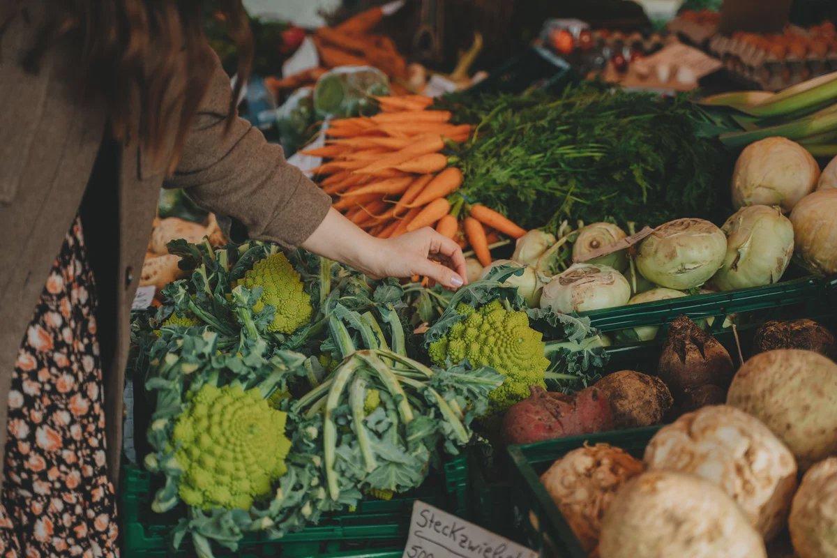 A shopper chooses vegetables at an outdoor produce stall.